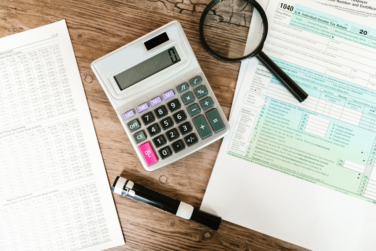 The Art of Drawing Readers In: Your attractive post title goes here Top view of tax forms, a calculator, and a magnifying glass on a wooden surface, ideal for accounting themes.